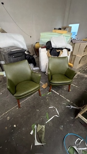 Two green upholstered armchairs with curved arms and wood legs photographed in the US Booths workshop for Modern Manor