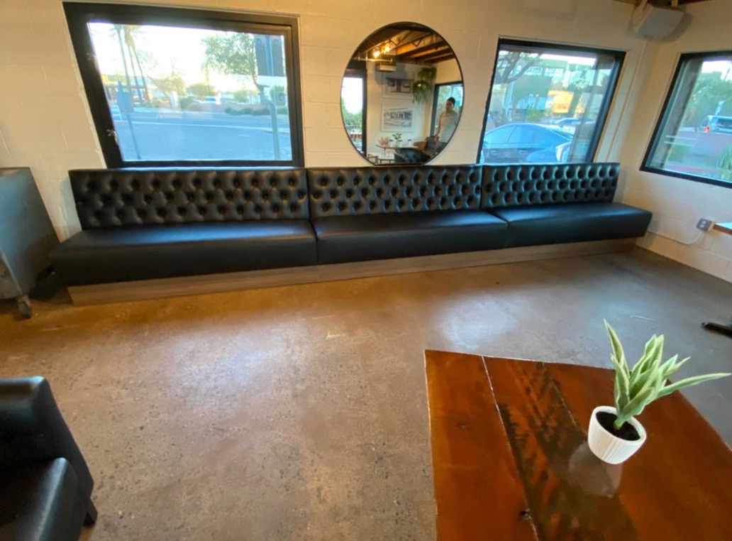 Black tufted banquette with smooth seats and a wood-front base beside the windows at Sip Coffee in Phoenix